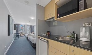 A modern hotel room with a kitchenette, a bed, a small table, and a view of the city.