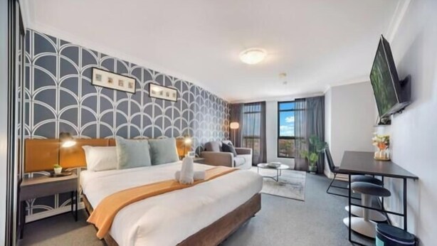 Une chambre d’hôtel avec un grand lit, un bureau, une chaise, une télévision et une fenêtre avec des rideaux.