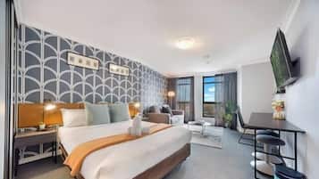 A hotel room with a large bed, a desk, a chair, a TV, and a window with curtains.