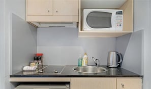 Una kitchenette compacta con microondas, lavaplatos y hervidor.