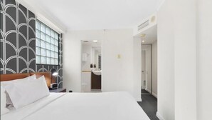 Habitación de hotel con una cama grande, una mesita de noche, un diseño moderno en la pared y un baño visible a través de una puerta abierta.