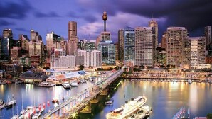 A city skyline with a prominent tower, a marina with boats, and a bridge connecting two areas.