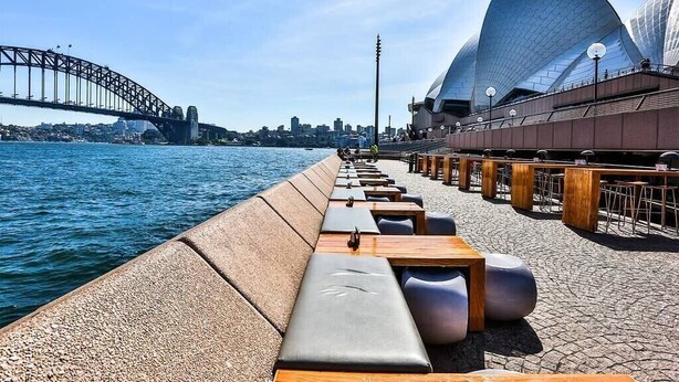 A waterfront promenade with seating and a view of the Sydney Opera House and Harbour Bridge.