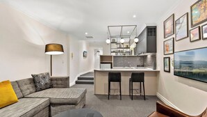 A modern living room with a sofa, a coffee table, and a TV. There is a kitchen area with a bar and stools.