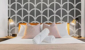 A neatly made bed with striped pillows, a white towel, and a headboard with a geometric pattern.