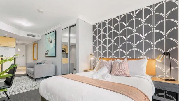Una habitación de hotel moderna con una cama grande, un sofá gris, un escritorio y un diseño decorativo en la pared.