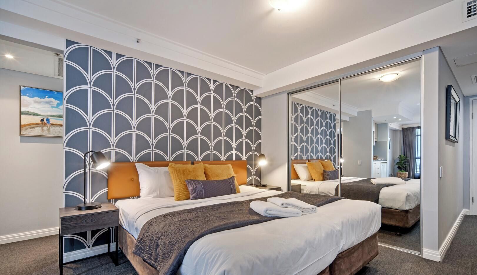 A hotel room with a large bed, a bedside table, a mirror, and a view of the hallway.