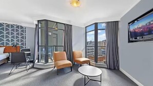 Une chambre d’hôtel dotée d’un coin salon, d’un téléviseur à écran plat et d’une grande fenêtre donnant sur la ville.