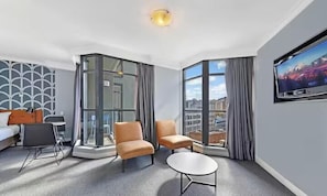 Une chambre d’hôtel dotée d’un coin salon, d’un téléviseur à écran plat et d’une grande fenêtre donnant sur la ville.
