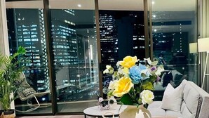 A modern living room with a city view, a dining area with black bowls and plates, and a vase with flowers. - Haymarket Prime Location Charming 2 Bed (Haymarket)