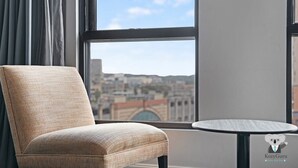 Ein Zimmer mit Blick auf eine Stadtlandschaft durch große Fenster, ein Sessel und ein kleiner runder Tisch.