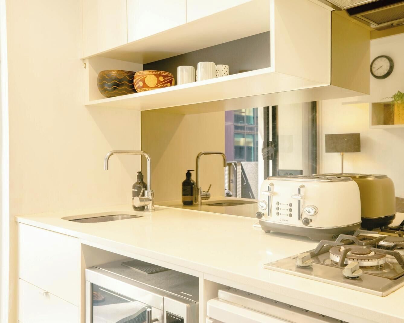 A modern kitchen with a sink, a toaster, a gas stove, and a dishwasher. There are shelves above the counter with decorative items.