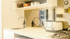 Una cocina moderna con un lavamanos, un tostador, una estufa a gas y un lavavajillas. Hay estantes sobre la encimera con objetos decorativos.