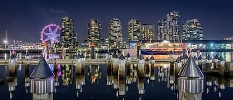Un paisaje urbano frente al agua con modernos rascacielos, una noria y un barco amarrado al muelle.