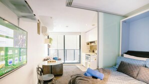 Una habitación de hotel moderna con balcón, un escritorio, una cama con ropa de cama estampada y una pantalla grande que muestra una interfaz de redes sociales.