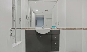 Un bagno con box doccia in vetro, lavandino bianco, mobiletti scuri e uno specchio.