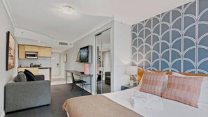 A hotel room with a bed, a desk, a chair, a sofa, a TV, and a kitchen area. - KozyGuru | Haymarket | Bright City Studio (Haymarket)