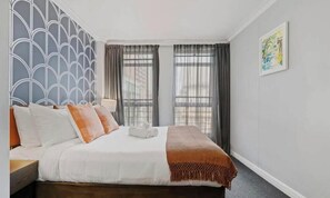 Une chambre d’hôtel avec un lit, des rideaux, un mur orné d’un motif géométrique et un tableau encadré.