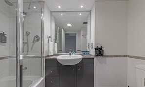 A modern bathroom with a glass-enclosed shower, a white sink, dark cabinets, and a mirror above the sink.