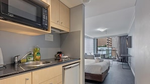 Una habitación de hotel compacta con kitchenette, una cama, un pequeño rincón de descanso y vistas a la ciudad.
