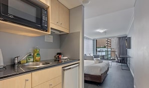Quarto de hotel compacto com cozinha compacta, uma cama, um pequeno espaço de estar e vista para a cidade.