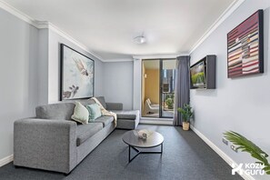 Ein modernes Wohnzimmer mit grauem Sofa, Couchtisch und einem Balkon mit Blick auf die Stadt.