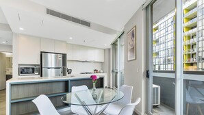 A modern kitchen with a glass dining table, white chairs, and a stainless steel refrigerator.