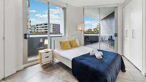 A modern bedroom with a bed, bedside table, and a view of a balcony.