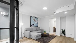 Una sala de estar moderna con un sofá seccional gris, una mesa redonda de centro, un cuadro en la pared y una planta en maceta.