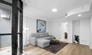 A modern living room with a grey sectional sofa, a round coffee table, a painting on the wall, and a potted plant.