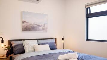 Une chambre à coucher avec un lit, des oreillers, une table de chevet avec une lampe, un climatiseur fixé au mur et une fenêtre donnant sur un paysage agréable.