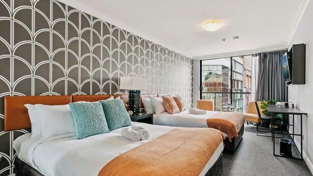 Ein Hotelzimmer mit zwei Betten, einem Schreibtisch, einem Fernseher und Blick auf die Stadt.