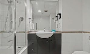 Une salle de bain avec une douche à parois de verre, un lavabo avec un miroir au-dessus et des toilettes.