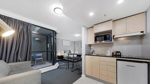 Una cocina moderna con microondas, estufa y refrigerador, un comedor con mesa y sillas, y una sala de estar con sofá y sillón.