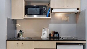 Una kitchenette compacta con microondas, cafetera y un refrigerador pequeño.