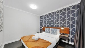 Una habitación de hotel con una cama, una mesita de noche, una lámpara y un papel tapiz estampado.