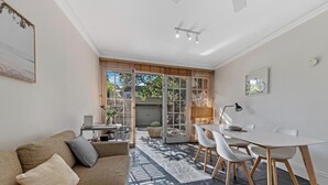 A compact living space with a dining area, a sofa, and a view through a glass door. - KozyGuru | Glebe | Cozy 2 Bedroom Terrace House (Glebe)