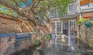 A brick wall, a tree, a metal bench, and a house with a glass door.