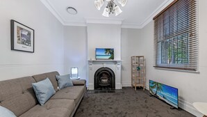 A living room with a fireplace, a sofa, a TV, and a bookshelf. - KozyGuru | Glebe | Cozy 2 Bedroom Terrace House (Glebe)
