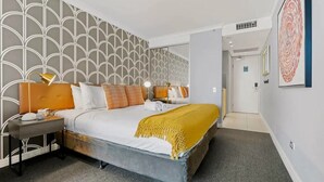 A modern hotel room with a large bed, a nightstand, a bedside lamp, and a wall with a geometric pattern.