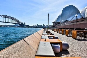 Eine Uferpromenade mit Sitzgelegenheiten und Blick auf das Sydney Opera House und die Harbour Bridge.