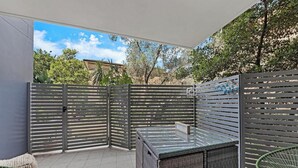 A covered patio area with a seating arrangement, a glass table, and a metal fence. - KozyGuru | Ryde | Cosy 2Bed Apt with Private Yard (Ryde)
