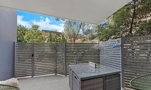 A covered patio area with a seating arrangement, a glass table, and a metal fence. - KozyGuru | Ryde | Cosy 2Bed Apt with Private Yard (Ryde)
