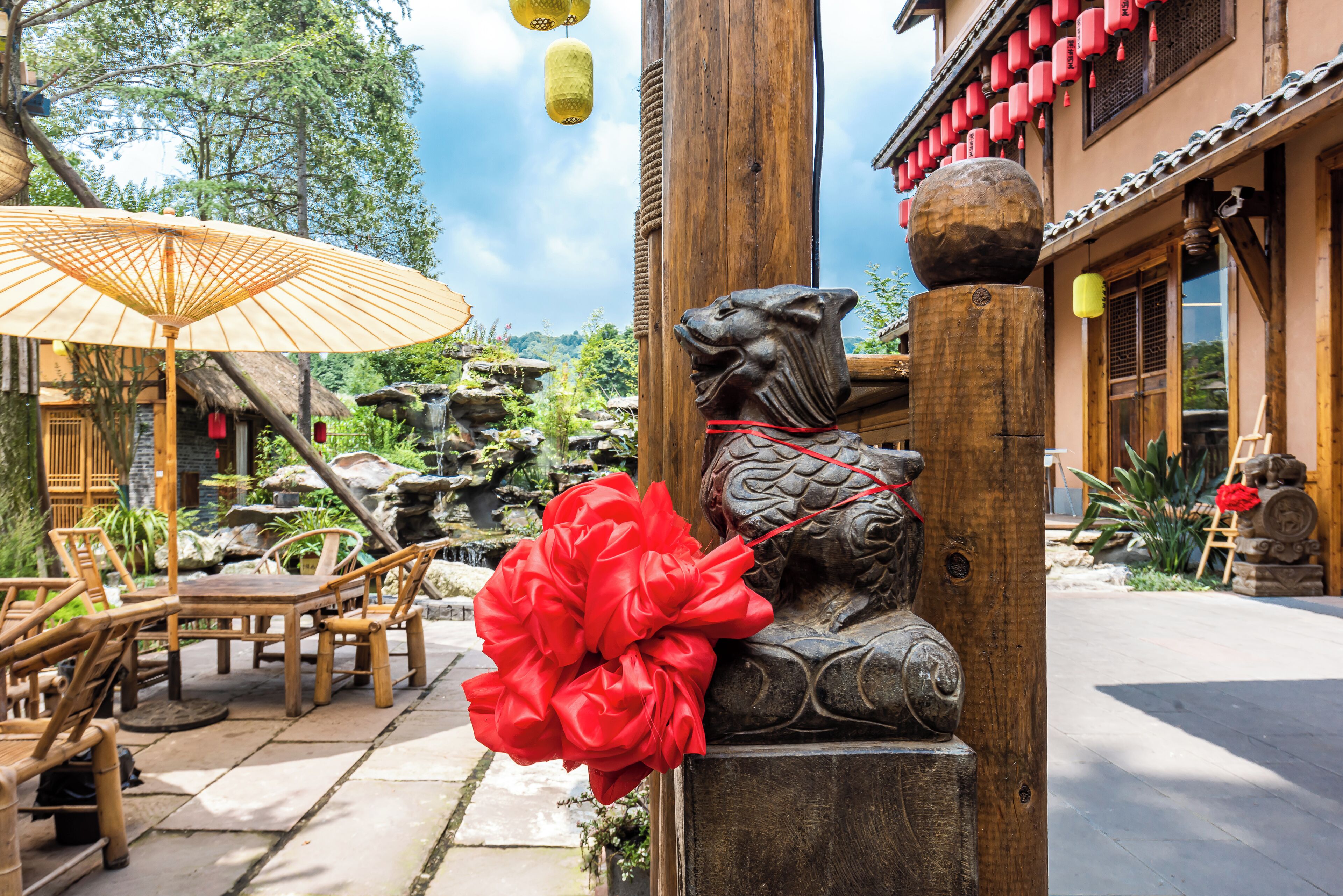 A traditional wooden building with a lion statue, outdoor seating, and a decorative red flower.
