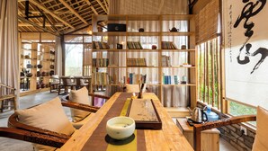 Une pièce de style japonais traditionnel, avec un sol recouvert de tatamis, une petite table sur laquelle est posé un bol, et une bibliothèque remplie de livres et d’objets décoratifs.