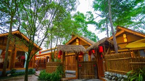 Un bâtiment traditionnel en bois, doté d’un toit de chaume, entouré d’une végétation luxuriante et bordé d’un sentier en pierre.