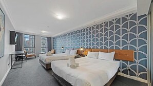 Ein Hotelzimmer mit zwei Betten, einem Schreibtisch, einem Sessel und einem großen Fenster.