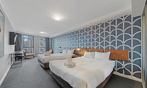 Une chambre d’hôtel avec deux lits, un bureau, une chaise et une grande fenêtre.