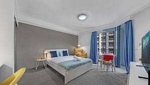 Ein modernes Hotelzimmer mit einem Bett, einem Schreibtisch, einem Sessel und einem Fernseher.