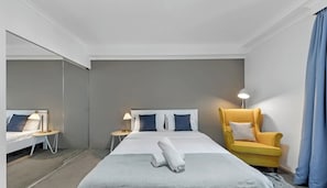 Ein Hotelzimmer mit Bett, Nachttischen, einem Sessel und einem Spiegel.